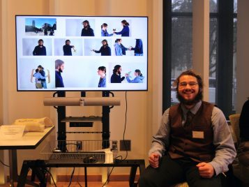 Paul Emery sitting by a screen with his project, "Augmented Interactions: Cardboard Emotes."
